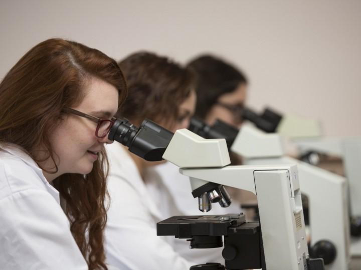 Three women in shite coats using microscopes to examine slides